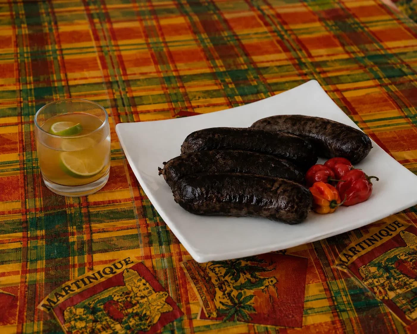 Trois boudins noirs brillants, piments bonda man Jacques rouges et oranges, nappe madras de la Martinique